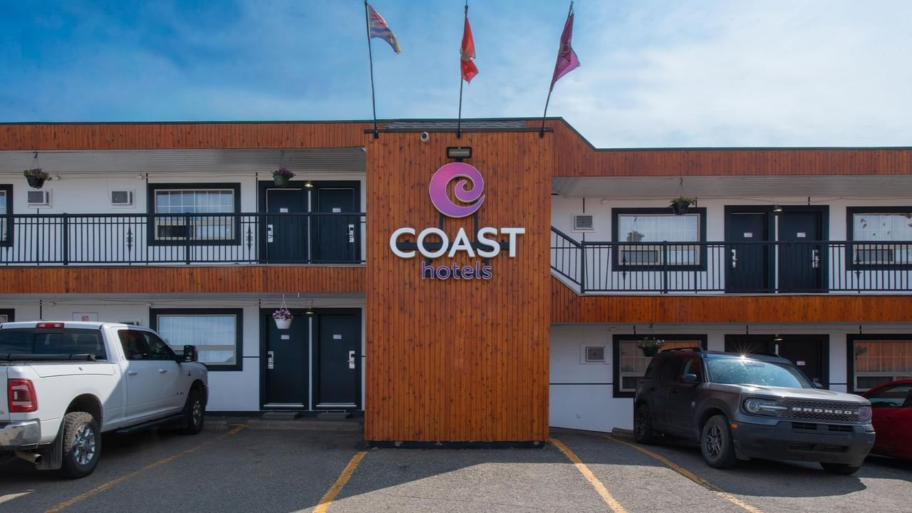 Exterior of Coast Dawson Creek Hotel with the Coast Hotels sign, guest room entrances and parked vehicles