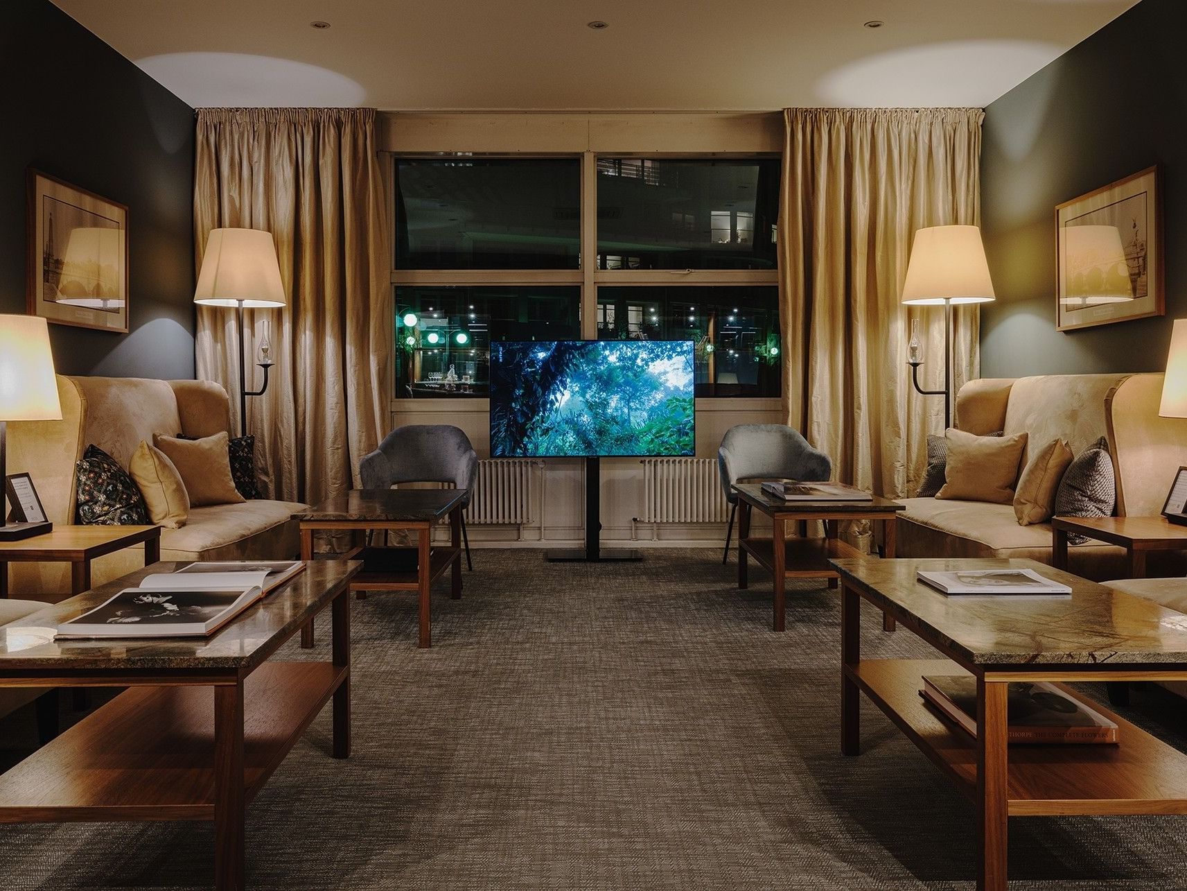 Ein gemütliches Wohnzimmer mit Sofas, Tischen, einem Flachbildfernseher und großen Fenstern mit Vorhängen.