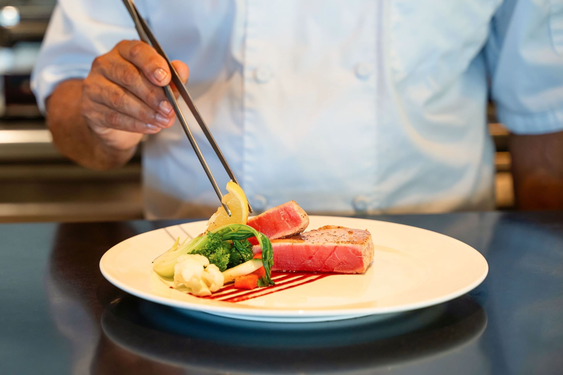 Chef placing a lemon slice on seared tuna and vegetables with chopsticks at Breeze Restaurant, Golden Rock Resort