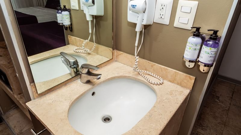 Wash basin, soap dispensers, hair dryer & silver faucet in a room at Gamma Puebla Senorial Centro