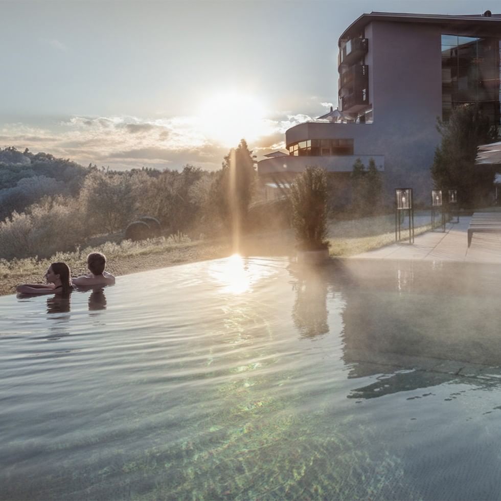 Zwei Gäste entspannen im Pool bei Sonnenuntergang am Falkensteiner Balance Resort Stegersbach.