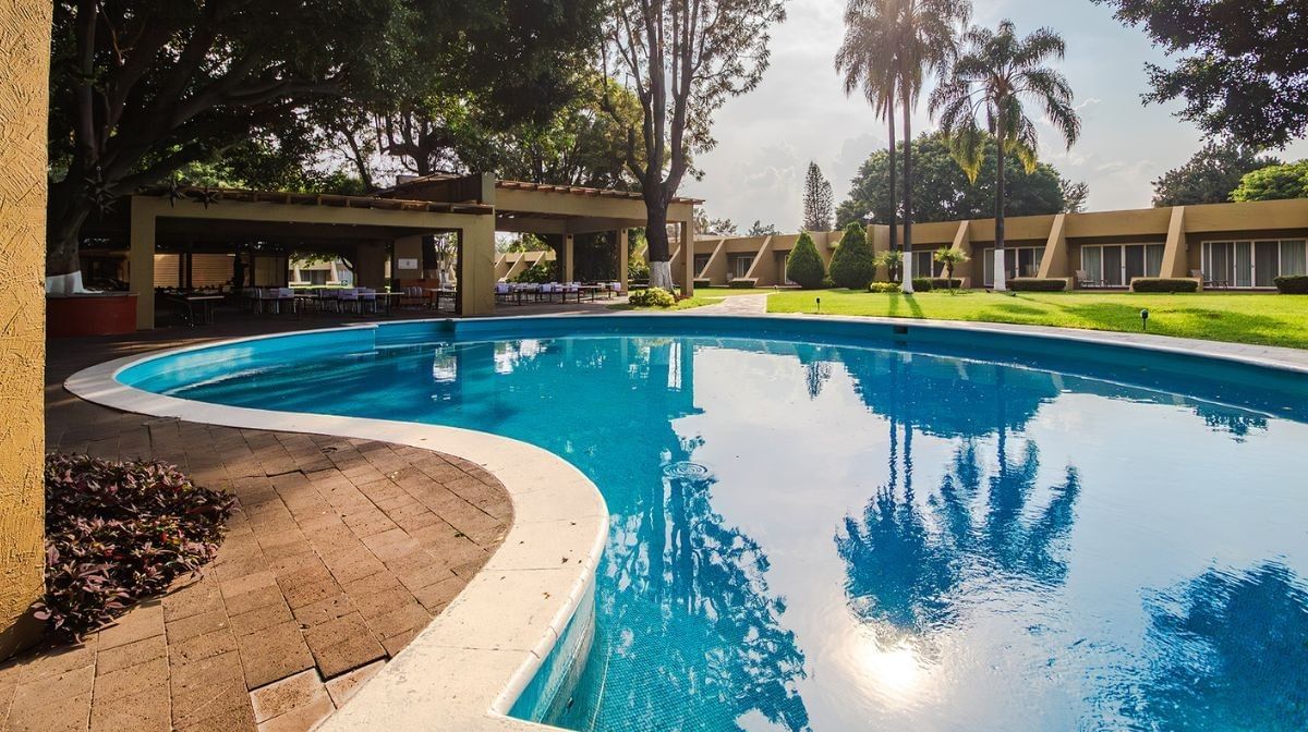 Curved pool by a brick patio under tall palm trees surrounding a green lawn at Camino Real Pedregal Mexico