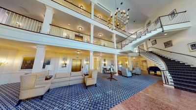 Spacious grand lobby with elegant grand staircase beside comfortable seating and chandelier at Avon Old Farms Hotel