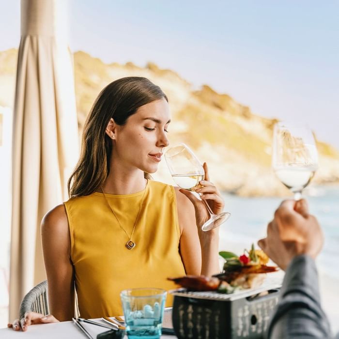 Woman holding wine glass at seaside restaurant in Falkensteiner Resort Capo Boi