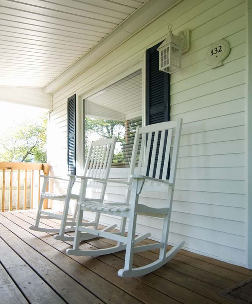 Two white rocking chairs sit on a wooden porch in Nick Cottage at Breezeway Boutique Hotel