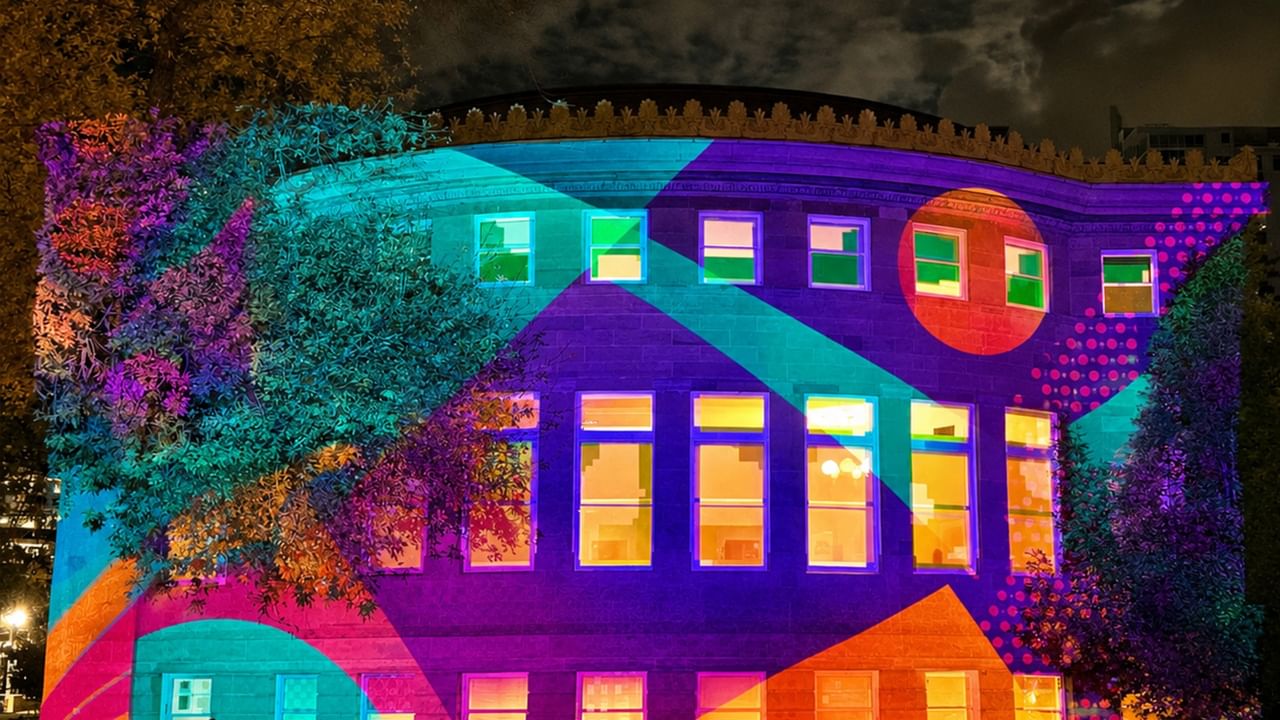 Building facade illuminated with vibrant purple, turquoise, orange, and pink geometric projections during Night Light event.