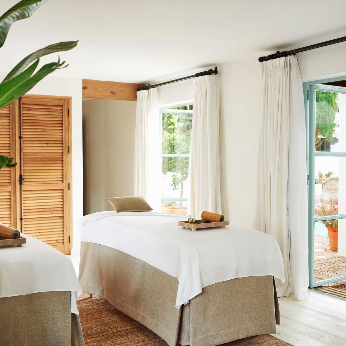 Dos camas de masaje listas en una sala con ventanas y cortinas en un spa.