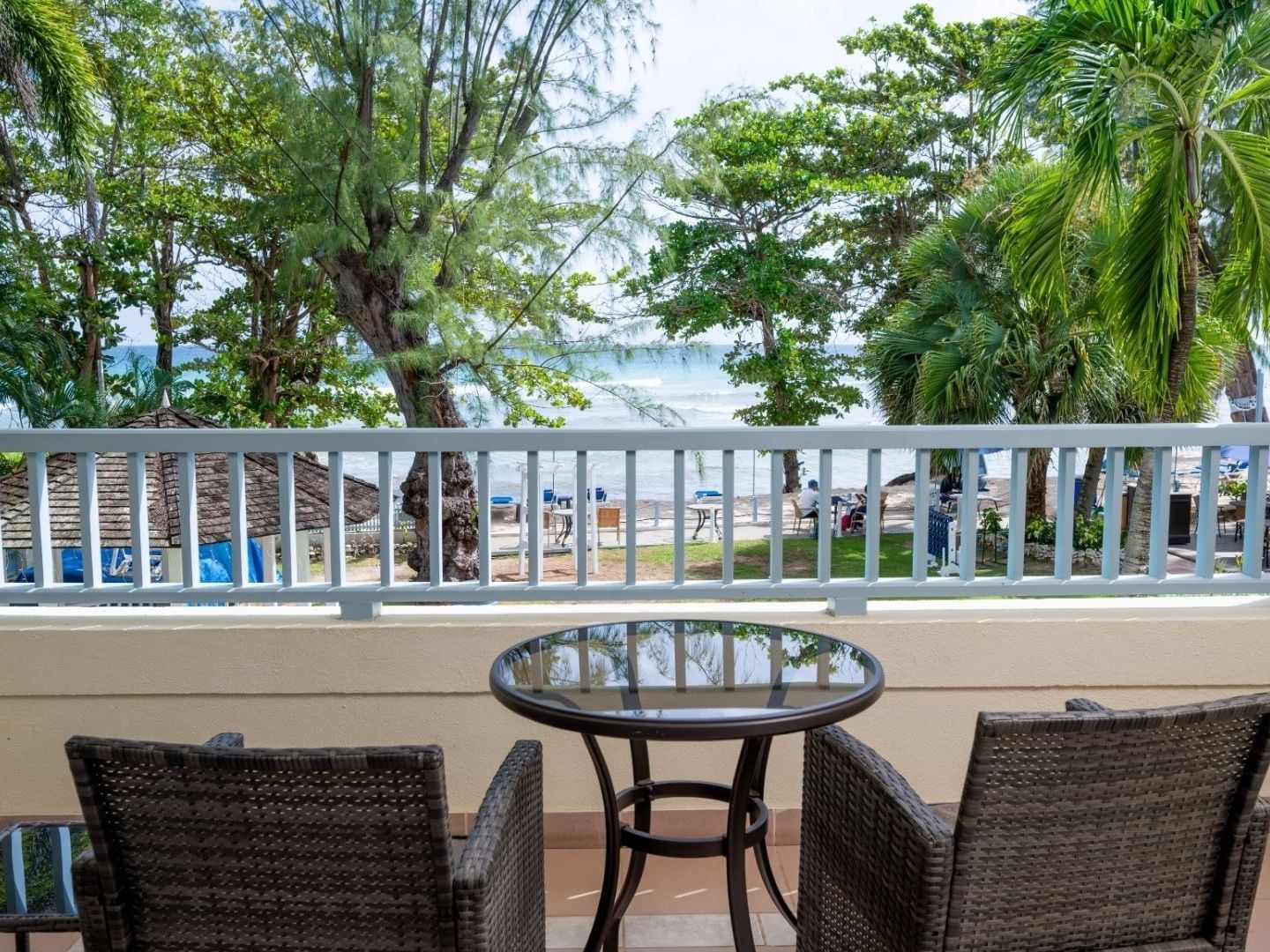 Two chairs and a glass table on a balcony overlooking the beach and trees.