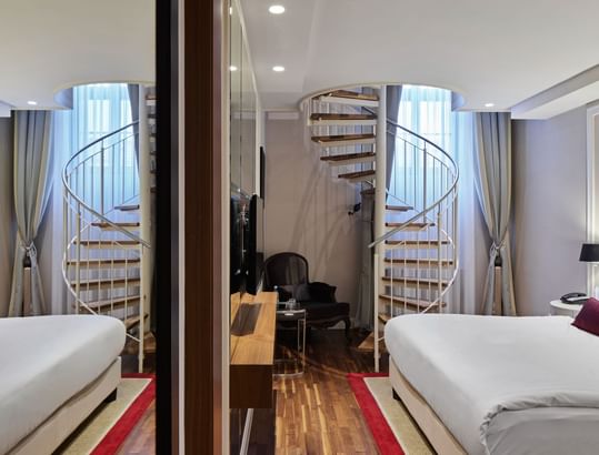 Titanic Duplex Suite's bedroom with twin beds and a spiral staircase at Titanic Gendarmenmarkt Berlin