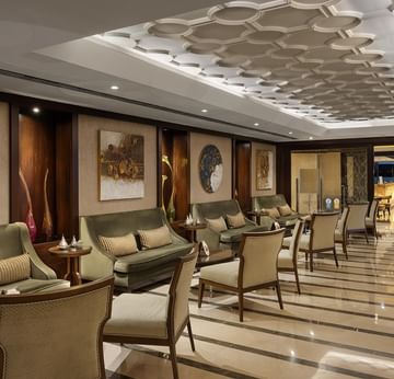 Elegant lounge area with green couches, cushioned chairs, decorative art, and a polished floor in Pascarella Restaurant Café & Bar.