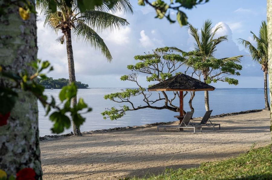 Two lounge chairs under a thatched umbrella on a quiet sandy beach overlooking the ocean at Warwick Le Lagon - Vanuatu