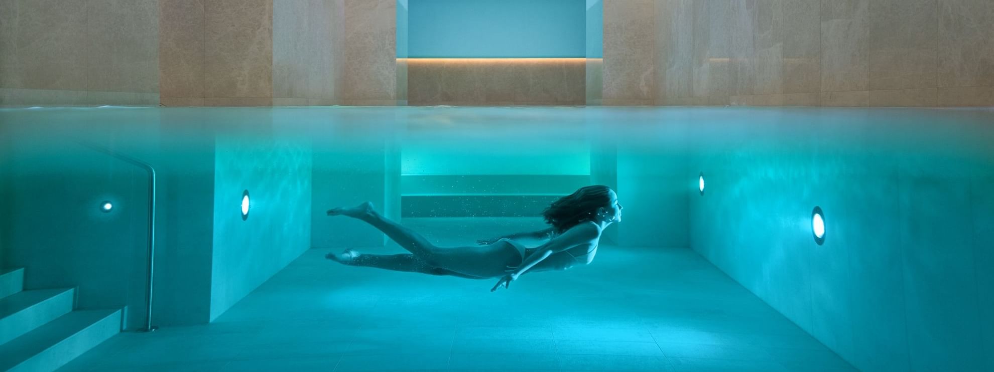 Person swimming in an indoor pool with blue lighting at Almanac Palais Vienna featuring Vienna hotel offers