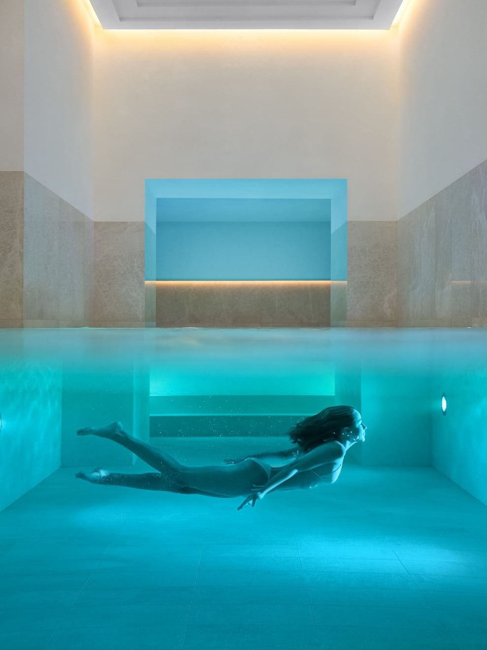 Person swimming underwater in a blue lighted outdoor pool at Almanac Palais Vienna