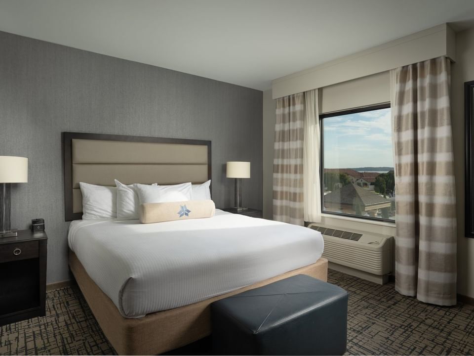 Nightstand and ottoman by the cozy bed in the King Room with carpeted floors at Shangri-La Resort and Golf Club