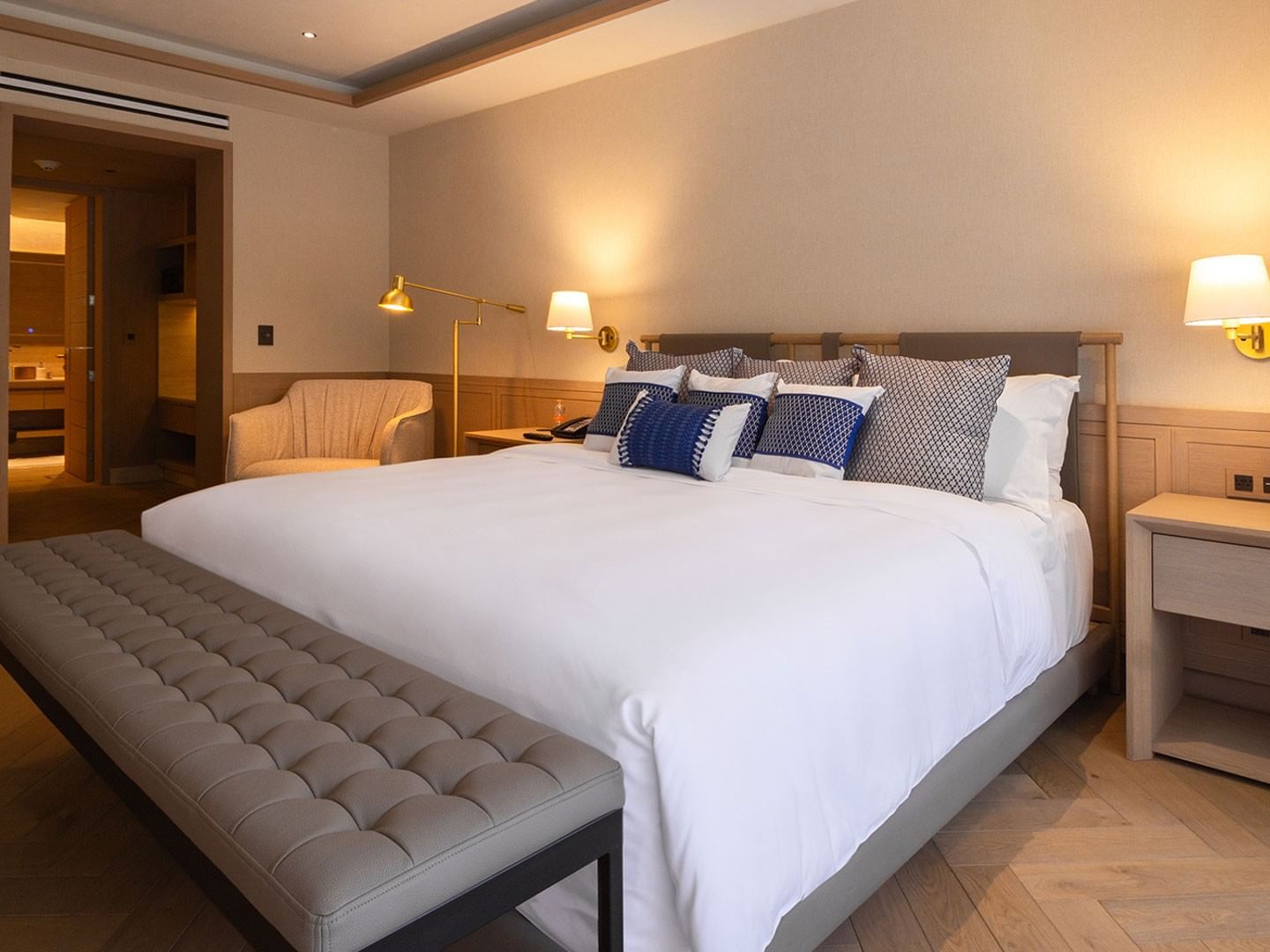 King Superior Viceroys Suite with blue accent pillows, a grey bench, and warm bedside lighting at Camino Real Polanco Mexico