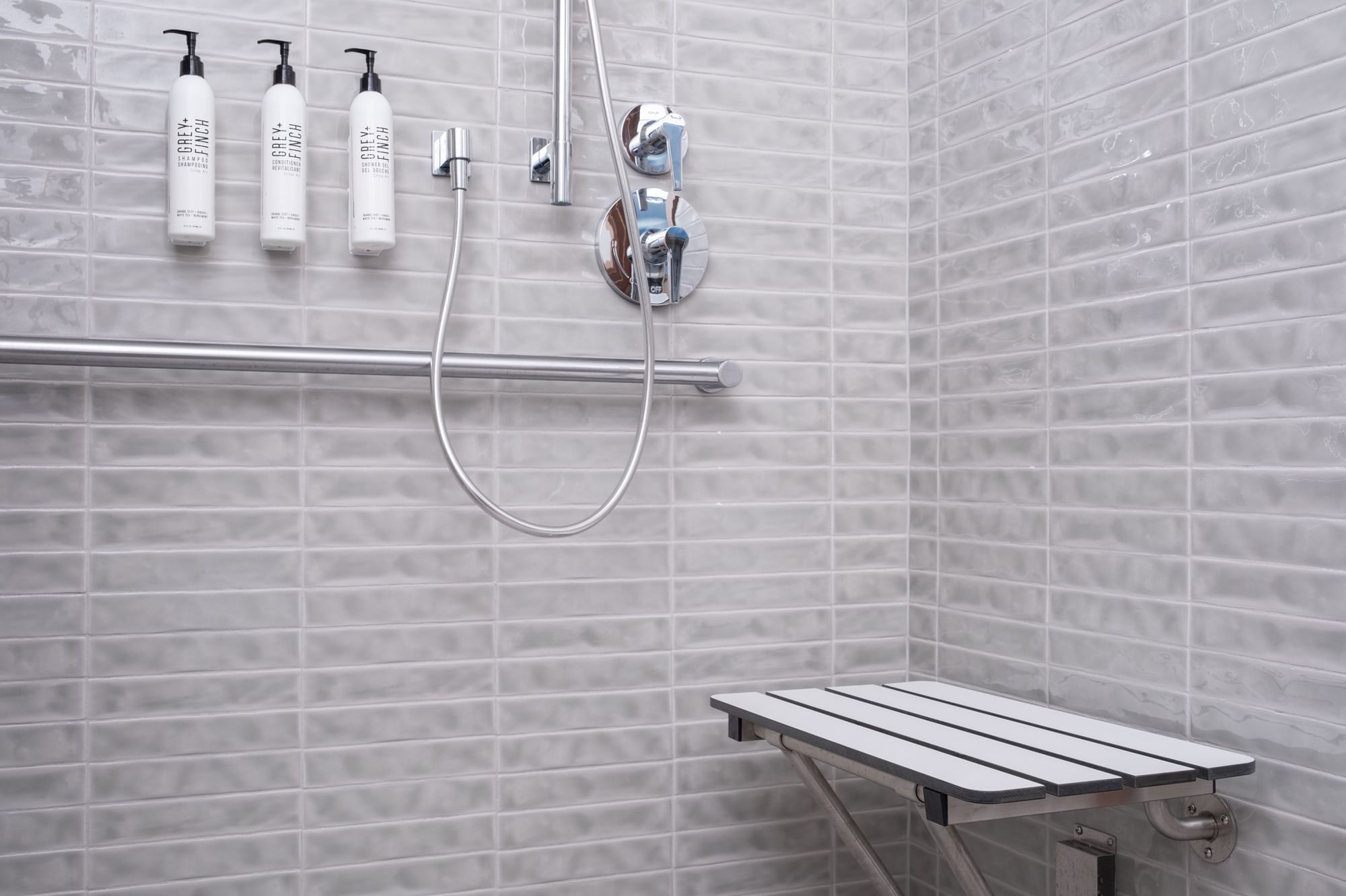 A clean and modern shower with a bench, grab bar, and amenities.