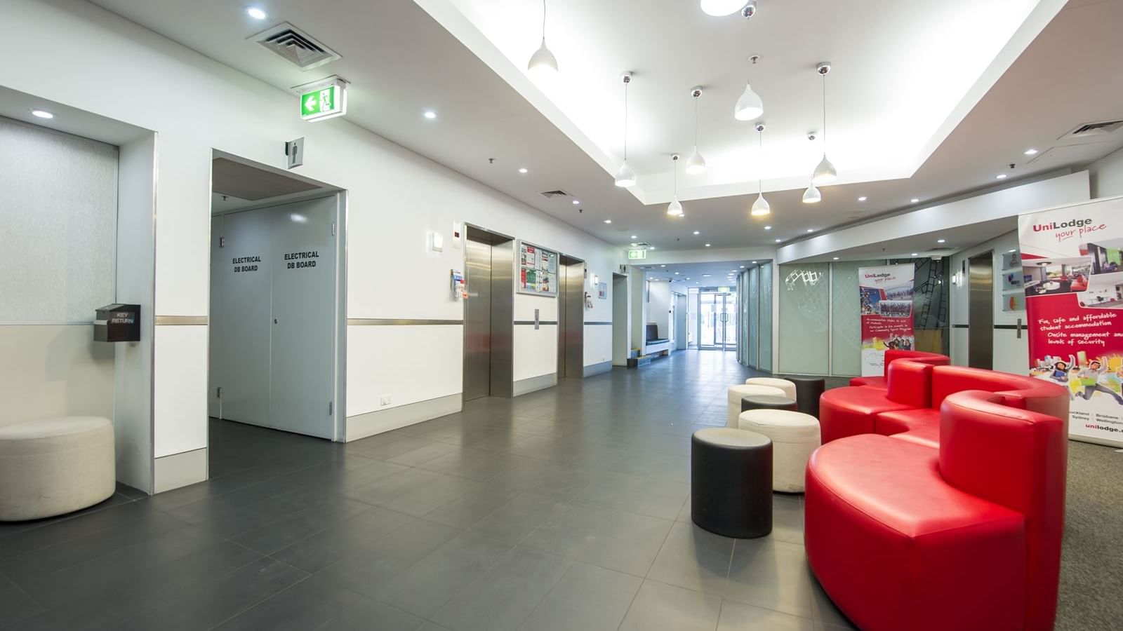 Modern lobby with red and beige seating, pendant lighting, and elevator access at StudentLiving - on Margaret