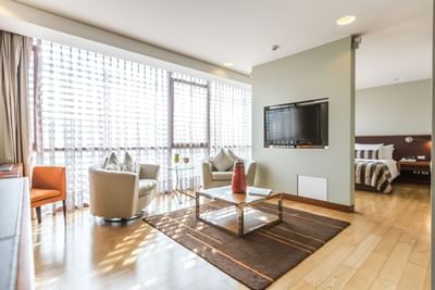 Sala de estar con TV junto a sillones cerca del dormitorio en Junior Suite de NOI Vitacura en Santiago, Chile