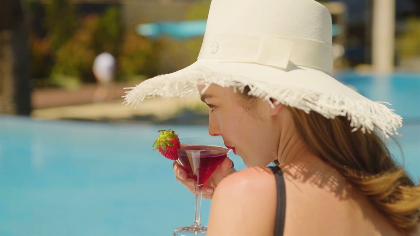 A lady having a cocktail by the pool at Crown Hotels