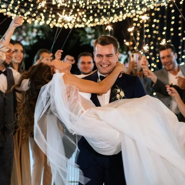 Bride in grooms arms having fun and surrounded by guests holding sparklers, a great new years eve wedding idea