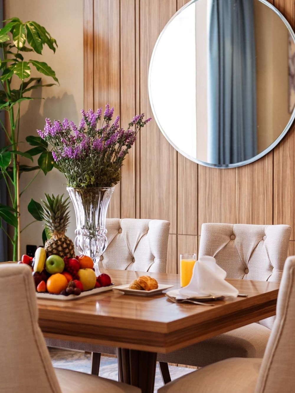 Purple flowers and a fruit platter on a wooden table by tufted chairs in Royal Suite at Cantonal Hotel by Warwick Riyadh