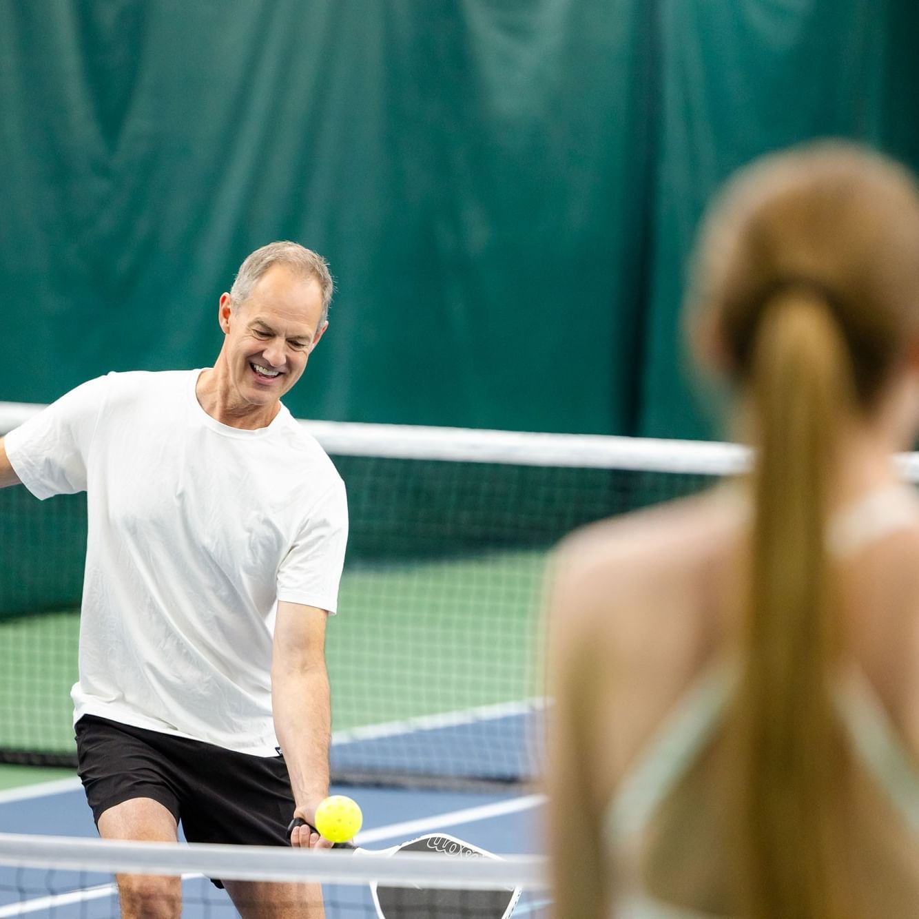 Man smiling and playing pickleball with a woman on a tennis court during Coed Intermediate to Advanced Pickleball Open Play.