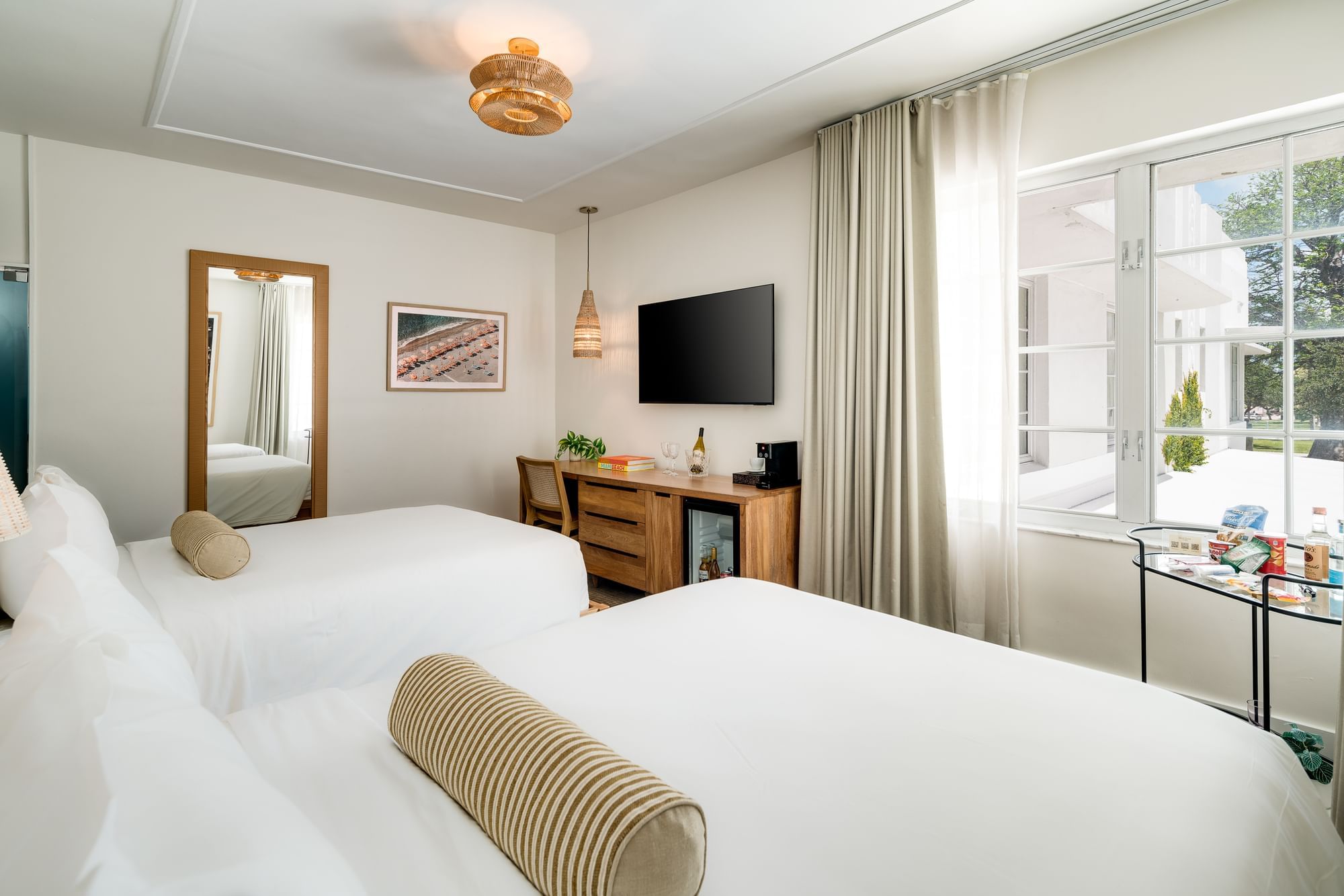 A hotel room with two beds, a desk, a TV, and a window.