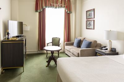 Brown television console sits by a round wooden table near a beige sofa in Standard Room Queen at Rodd Charlottetown Hotel