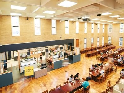 People dining at long tables in a large room at La Trobe University - Glenn College.