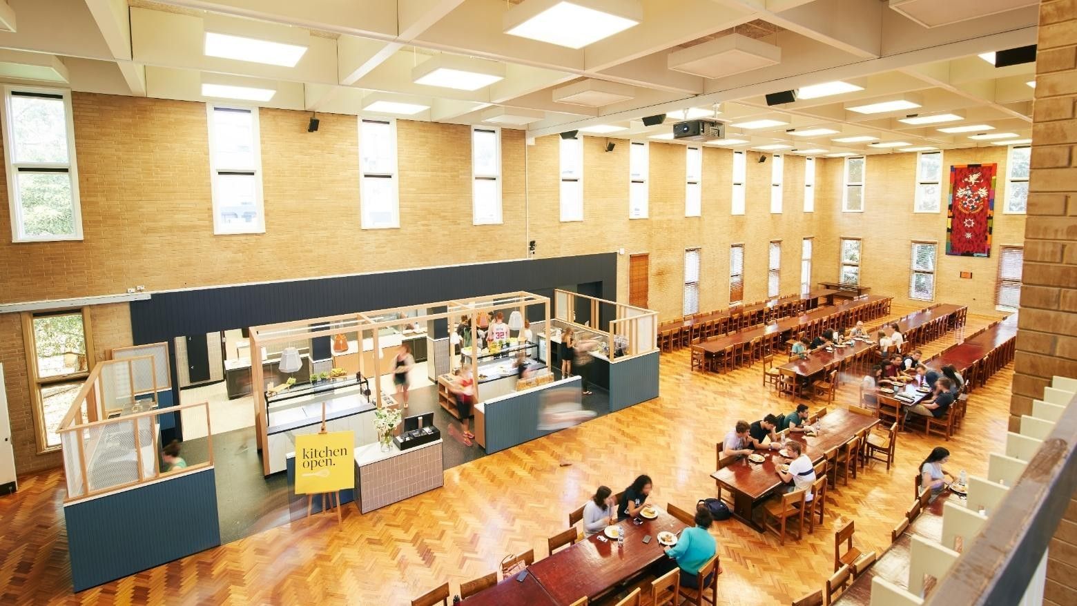 People dining at long tables in a large room at La Trobe University - Glenn College.