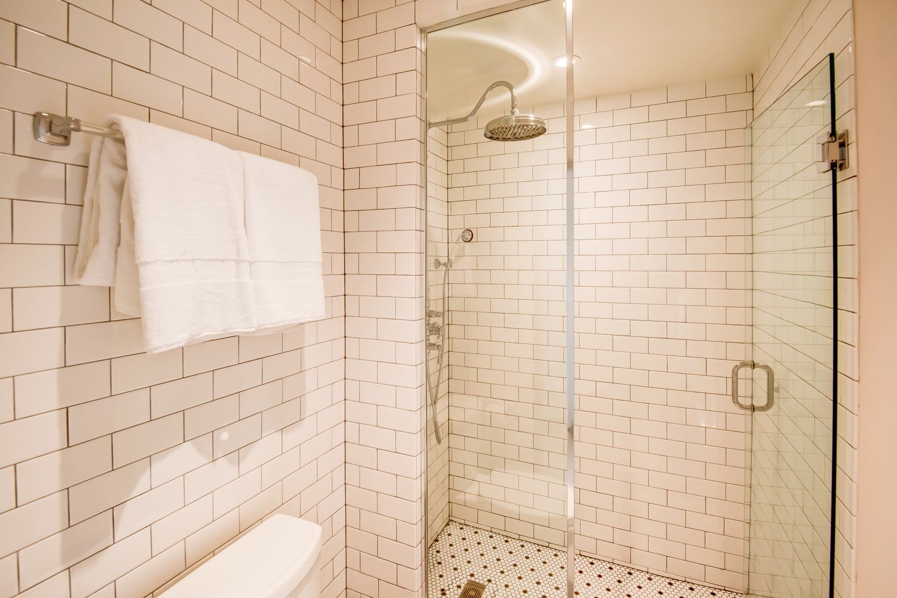 A bathroom with a glass-enclosed shower, white subway tile walls, and a towel rack with white towels.