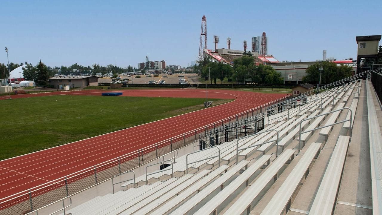 Stadium seating and red running track with green field at Foothills Athletic Park under clear blue sky.