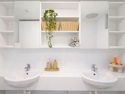 Modern white bathroom with two sinks, a mirrored cabinet, and baskets at UniLodge at Curtin University Guild House.