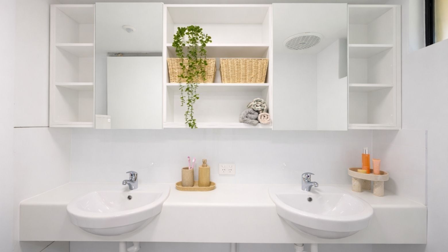 Modern white bathroom with two sinks, a mirrored cabinet, and baskets at UniLodge at Curtin University Guild House.