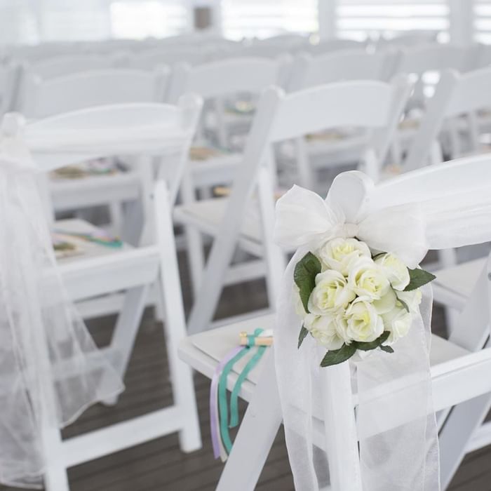 White folding chairs adorned with ribbons and roses, set for a wedding ceremony at Mercure Hotel Townsville