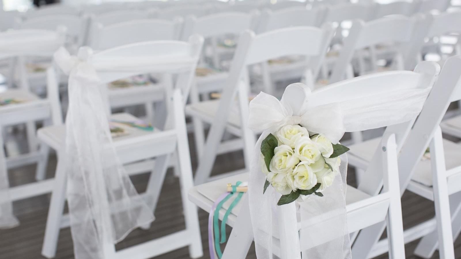 White folding chairs adorned with ribbons and roses, set for a wedding ceremony at Mercure Hotel Townsville