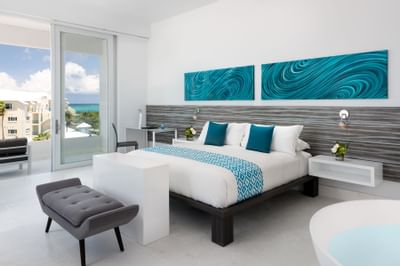 King bed with teal pillows and abstract wave art with balcony with ocean views in Penthouse Suite at Zenza Hotel