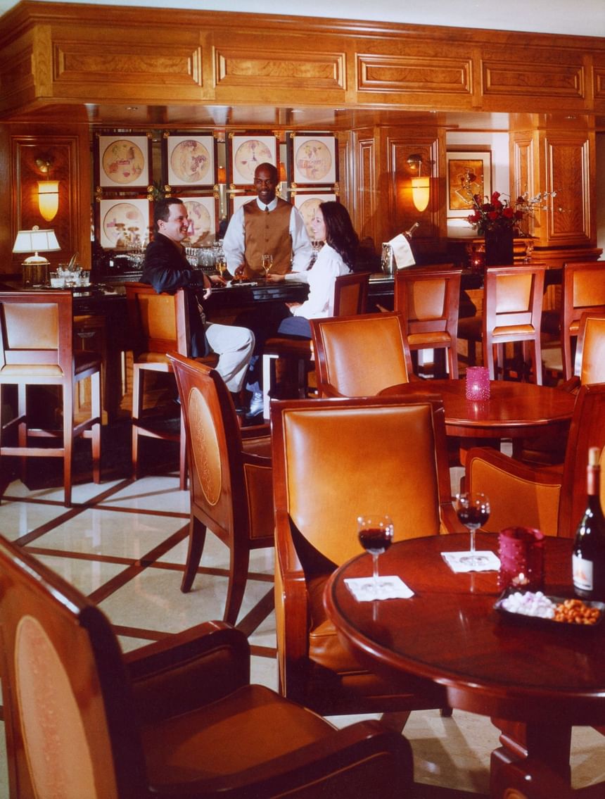 Luxurious bar scene with wooden decor, patrons enjoying drinks, and elegant furniture at The Rose Hotel