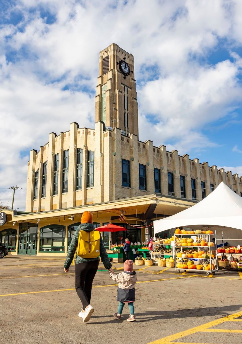 Adult and child walking toward historic clock tower building with outdoor market stalls at Warwick Le Crystal Montreal