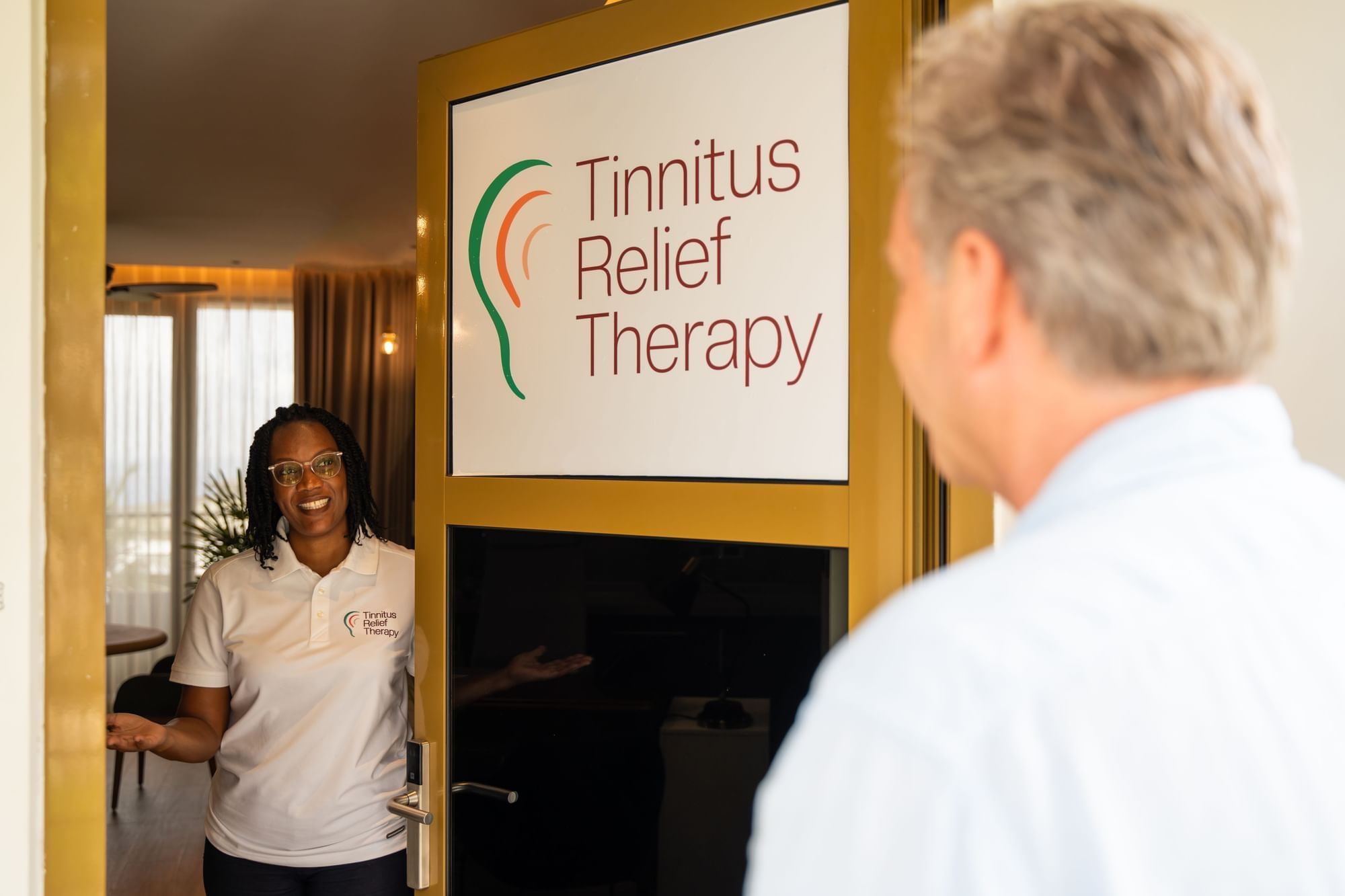 Smiling staff member welcoming a guest at the entrance of Tinnitus Relief Therapy room at Golden Rock Resort