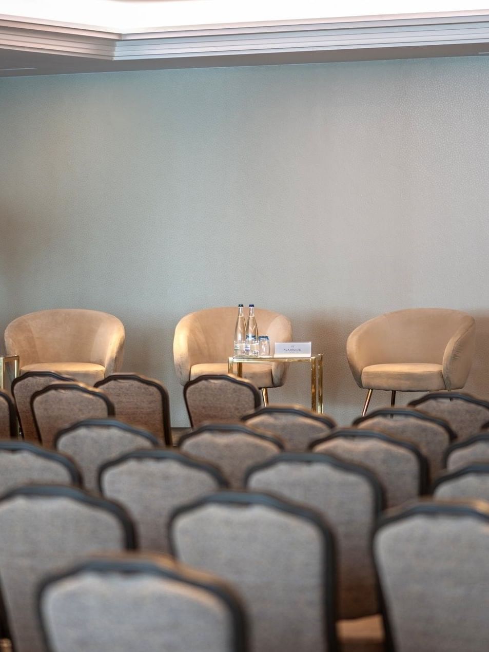 Beige armchairs by gold side tables on a stage facing rows of chairs in Mont-Blanc + Jura at Warwick Geneva