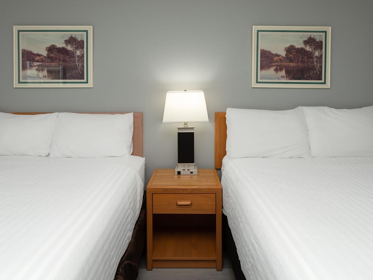 Two queen beds with white linens, wooden nightstand and framed artwork.