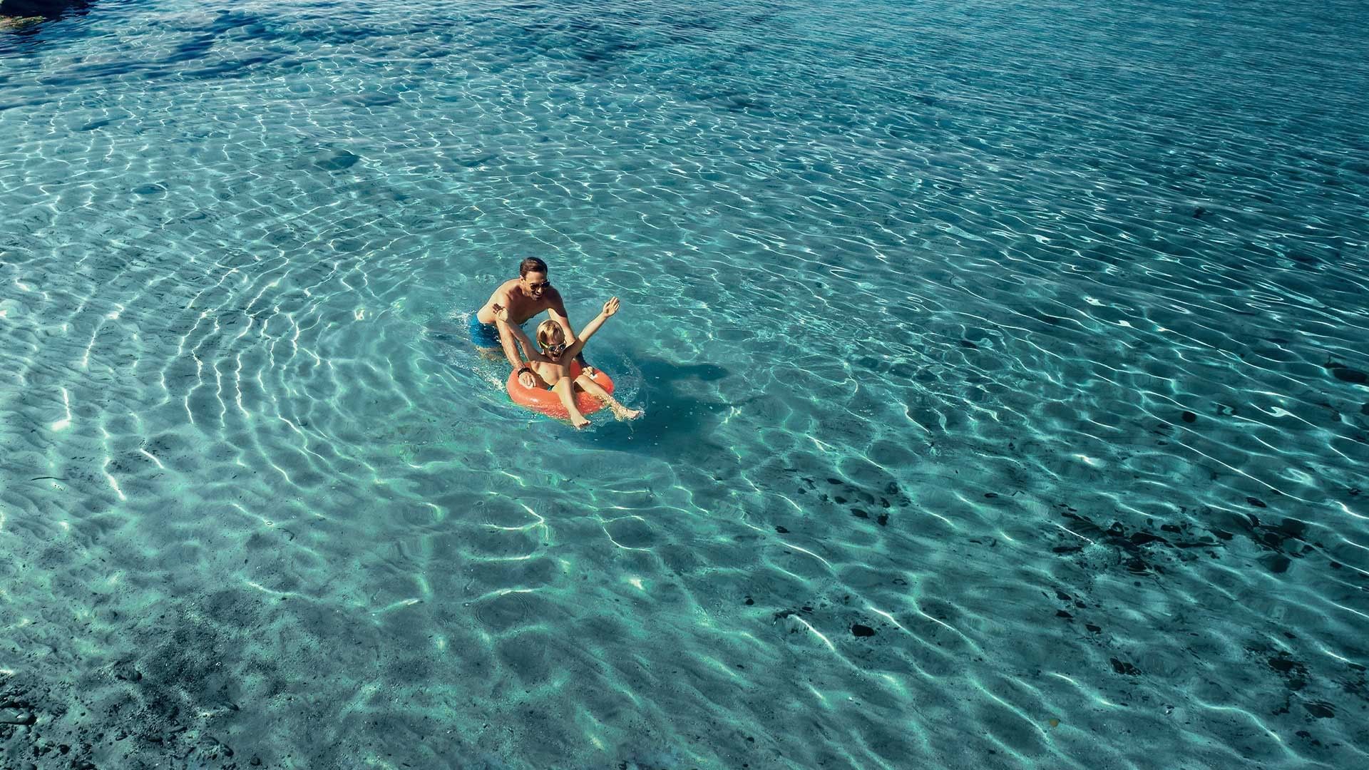 Coppia e bambino su un galleggiante in acqua cristallina a Falkensteiner Group