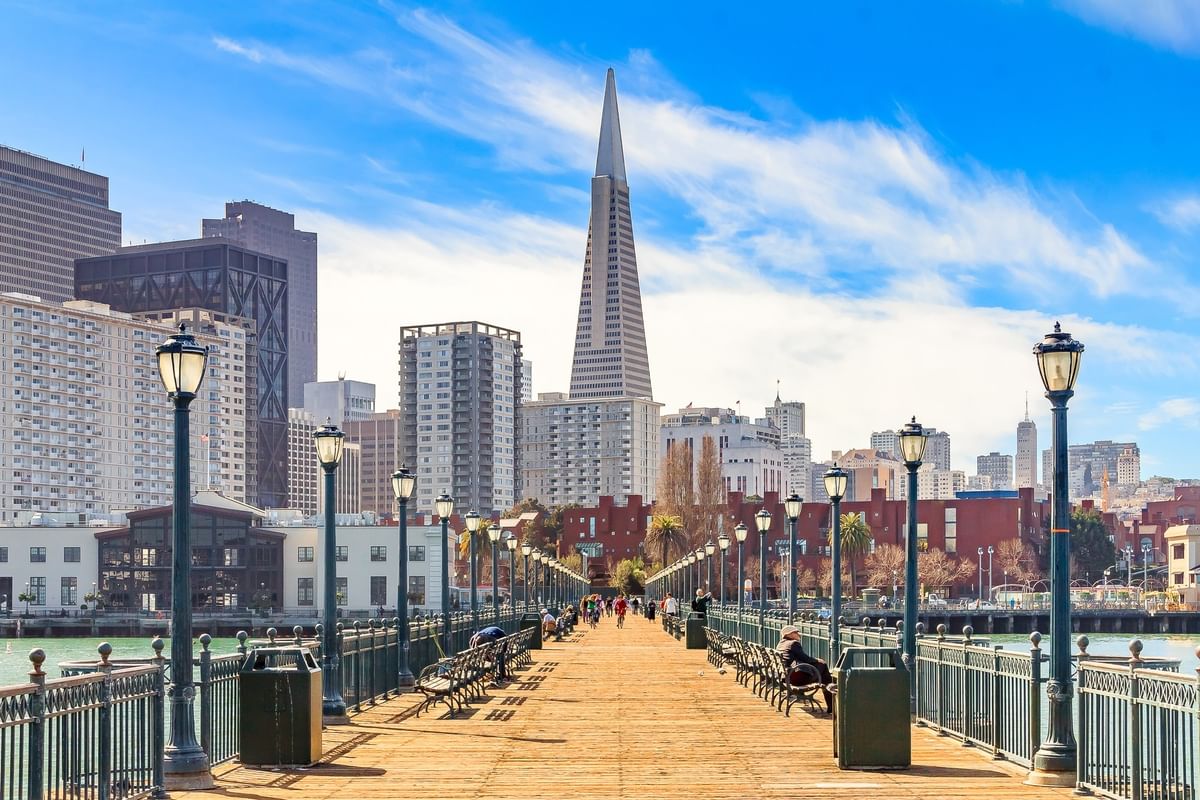 Wooden pier with lamp posts by a city skyline under a blue sky near Warwick San Francisco