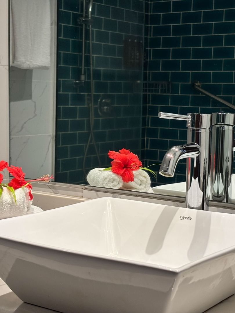 White square vessel sink by rolled towels featuring red hibiscus flowers at Warwick Hotels & Resorts