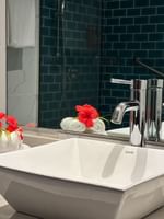White square vessel sink by rolled towels featuring red hibiscus flowers at Warwick Hotels & Resorts