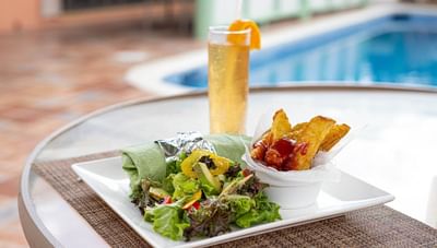 Green wrap with fresh salad & crispy French fries on table beside pool in Hott Pott Restaurant at Worthing Court Apartment