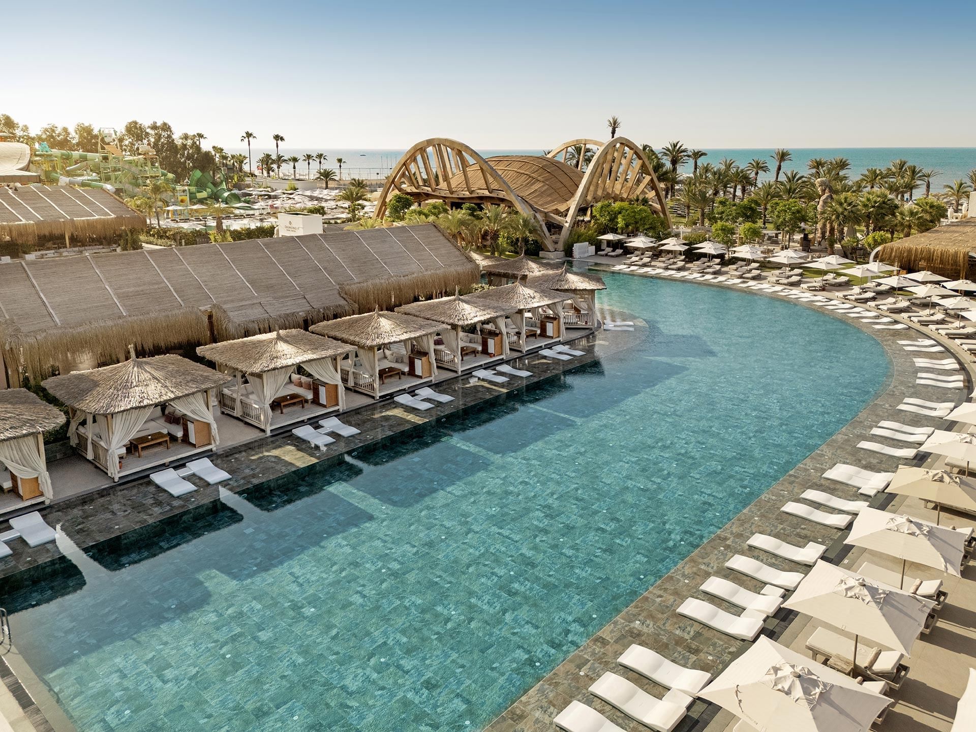 Cullinan Belek: A resort with a large pool, lounge chairs, umbrellas, and a scenic ocean view.