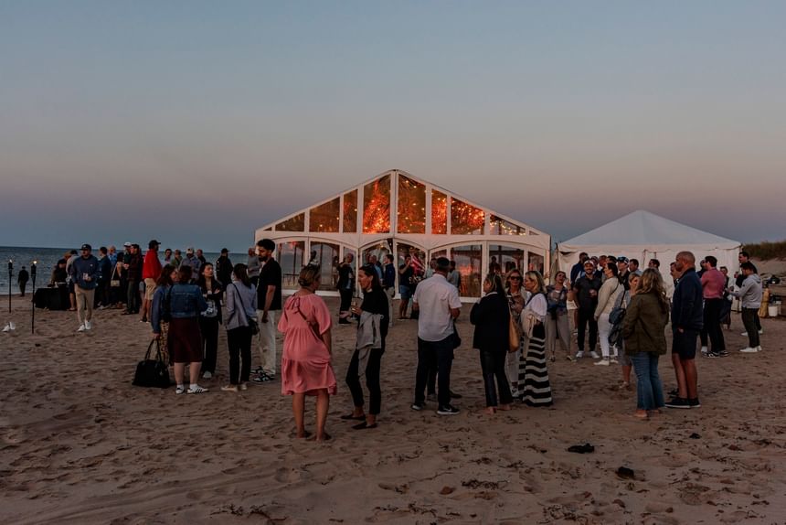 People mingling on the beach outside a lit tent during lively PEI events at Rodd Crowbush Golf & Beach Resort