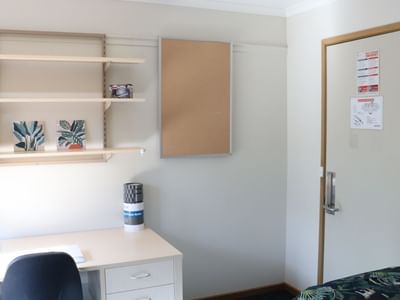 White room with desk, chair, shelf, and bed at La Trobe University - Terraces.